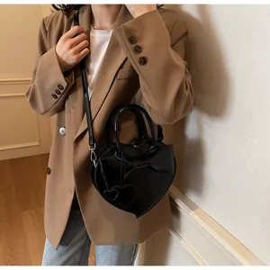 Detailed view of the heart-shaped glossy crossbody bag with bow and leather strap