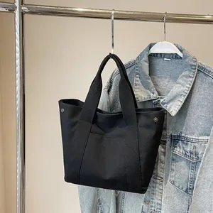 Close-up of black canvas tote bag showing front flat pocket and metal side snap buttons