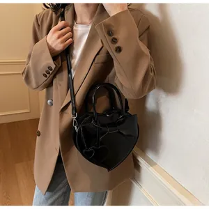 Detail of heart-shaped black crossbody bag with large bow and polished leather texture