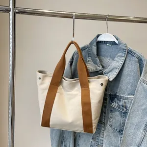Detail of off-white canvas tote bag featuring brown woven handles and metal ring accents