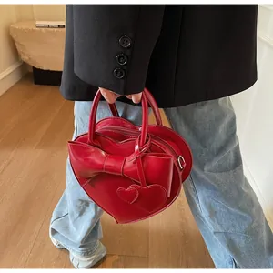 Close-up of a red heart-shaped leather handbag with a bow and dual heart charms