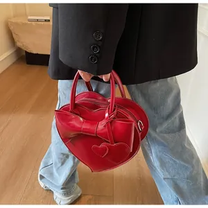 Detail of red heart-shaped shoulder bag with large bow and charms held by a model