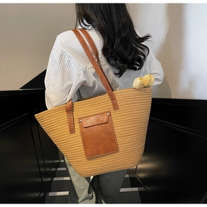 Detail of woven tote bag with brown leather straps and pocket on grey stairs