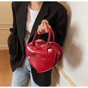 Detail of red heart-shaped patent leather shoulder bag with bow and charms on model