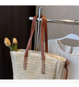 Close-up of handmade straw tote bag with brown leather handles and reinforced stitching