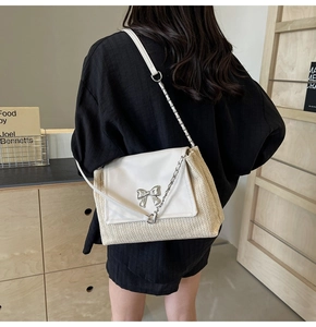 Détail du sac à bandoulière en paille tressée avec rabat en cuir blanc et nœud argenté