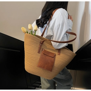 Close-up of woven tote bag with brown leather straps and front pocket detail