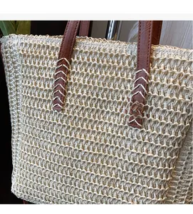 Detail of straw tote bag showing beige woven texture and leather handle with V-shaped stitching