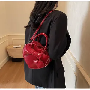 Detail of red heart-shaped shoulder bag with bow and charms worn over a black blazer