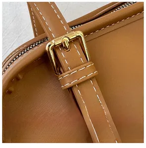 Dettaglio della borsa in pelle marrone con cuciture bianche e fibbia in metallo dorato