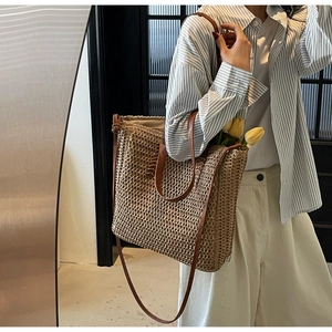 Close-up of a woven straw tote bag with brown leather handles and a long shoulder strap