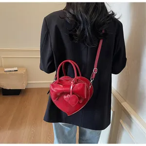 Red heart-shaped shoulder bag with bow and dual heart charms on a model in a black blazer