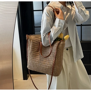 Close-up of beige woven straw tote bag featuring brown leather straps and spacious interior