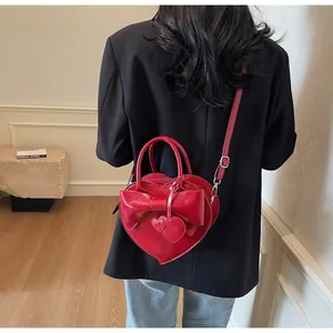 Detail of red heart-shaped shoulder bag with large bow and dual heart charms on a model