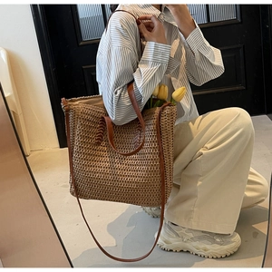 Detail of hand-woven straw tote bag featuring brown leather straps and floral accents
