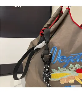 Détail du sac en nylon gris avec broderie Vegetable bleue et bordure rouge vive