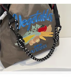 Détail de la broderie de légumes et du texte bleu sur le sac cabas en nylon