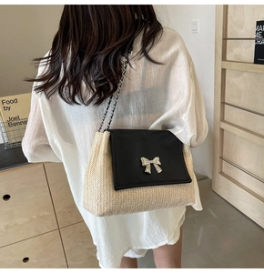 Détail d'un sac bandoulière en paille avec rabat en cuir noir et nœud argenté élégant