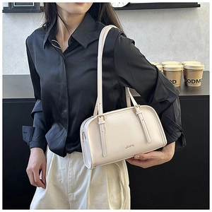 Dettaglio della borsa a cuscino in pelle beige con finiture dorate indossata sottobraccio