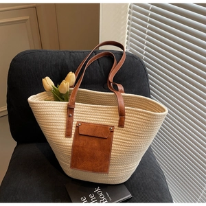 Detail of a beige woven tote bag with brown leather straps and front pocket on a chair