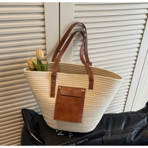Detail of woven tote bag with brown leather handles and front pocket on black seat