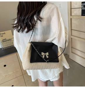 Détail du sac à bandoulière en paille avec rabat en cuir noir et nœud argenté sur modèle
