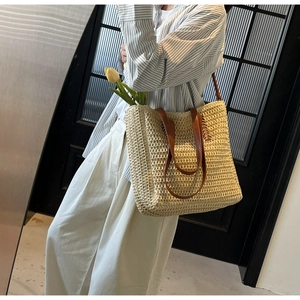 Close-up of beige woven straw tote bag featuring brown leather handles and shoulder straps
