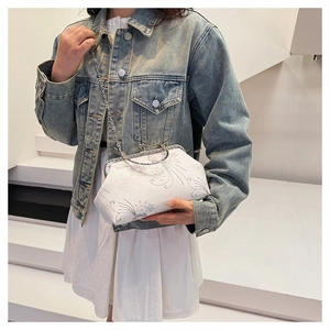Detail of white satin frame bag featuring floral embroidery and silver chain on model