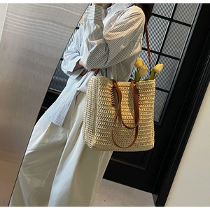 Detail of beige straw tote bag with brown leather straps and chic woven texture patterns