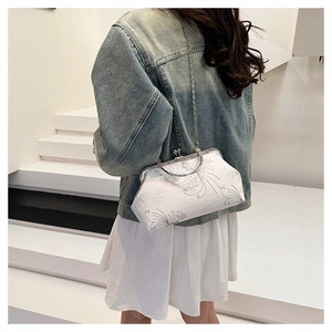 Detail of white vintage floral embroidery on kiss-lock crossbody bag with silver chain