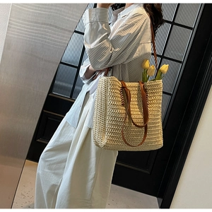 French style straw tote bag with brown leather handles worn by a model in a natural setting