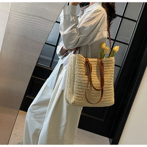 Detail of minimalist straw tote bag with brown leather straps and spacious interior