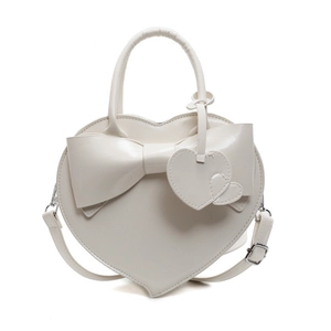 White heart-shaped handbag with large bow and adjustable shoulder strap on plain background