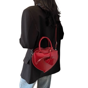 Red heart-shaped shoulder bag with bow detail shown on model in a white studio background