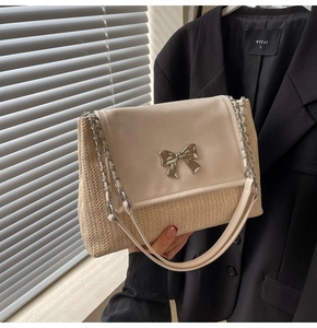 Détail d'un sac d'épaule en paille beige avec nœud en métal argenté et bandoulière