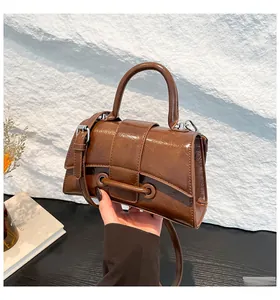 Close-up of brown glossy leather hourglass bag held by hand, showing shiny patent texture