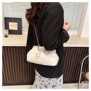 Detail of floral embroidery on white fabric bag with elegant metal frame and chain