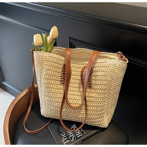 Detail of beige straw tote bag with brown leather straps and V-shaped stitching on wood chair