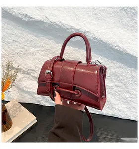 Close-up of deep red glossy hourglass handbag with top handle and adjustable shoulder strap