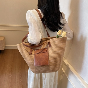 Straw woven tote bag with brown leather pocket shown on model in a minimalist setting