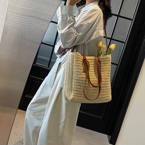 French style beige woven straw tote bag with brown leather handles worn by a model