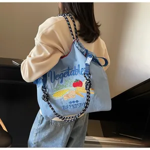 Détail d'un sac en toile bleu clair avec broderie de légumes colorés et bandoulière corde