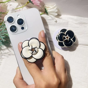 Detail of camellia flower phone grip with black outline and golden center on white smartphone