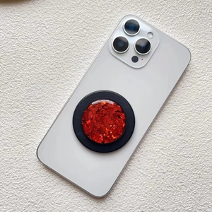 Detail of a red sequin circular magnetic folding phone grip on a white textured background