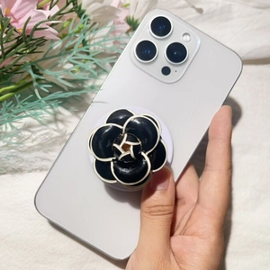 Close-up of a black camellia phone grip accessory with white petal edges on a smartphone