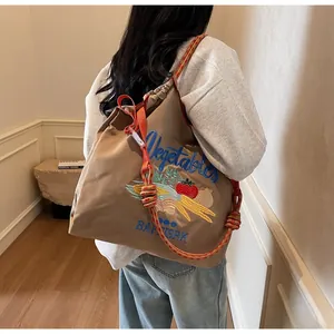 Détail du sac cabas en toile marron avec broderie légumes et bandoulière tissée orange