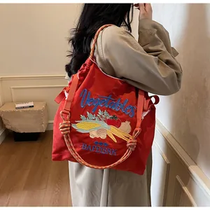 Détail de broderie légumes sur un sac bandoulière en nylon rouge avec bandoulière épaisse
