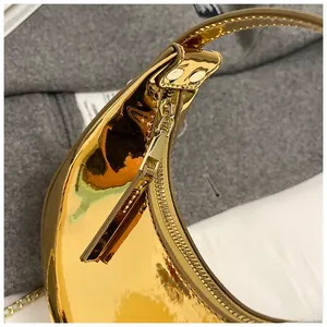 Close-up of golden patent leather crescent bag showing smooth surface and metal zipper