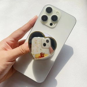 Macro shot of heart-shaped luxury mirror phone grip with gold frame on white smartphone