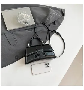 Top view of glossy black pleated leather hourglass bag with metal ring and shoulder strap